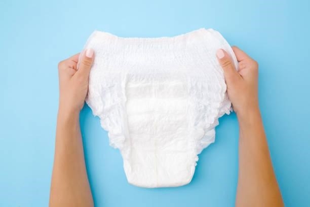 Woman hands holding white adult diaper on pastel blue background. Closeup. Point of view shot. Top view.